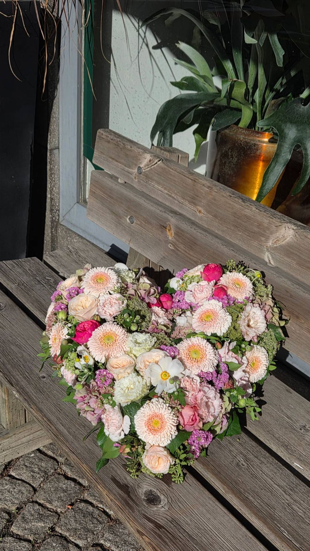 Trauergesteck in Herzform aus Rosen, Gerbera und Nelken auf einer Holzbank